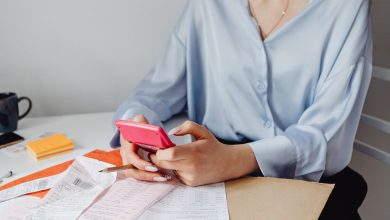 Mulher usa uma calculadora rosa entre contas e recibos sobre uma mesa.