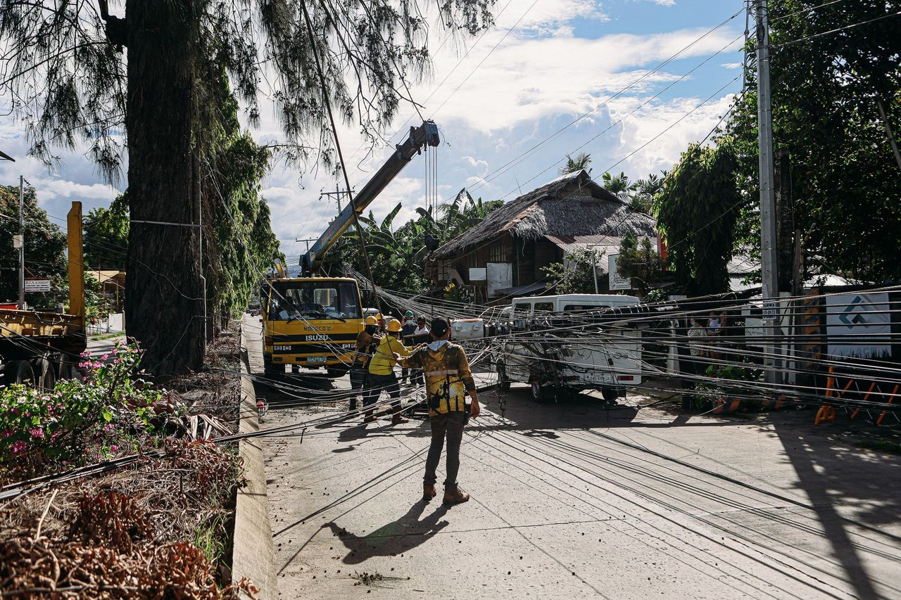 Trabalhadores consertam linhas de energia danificadas após uma tempestade em uma área tropical.