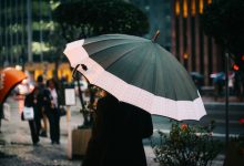 Pessoa caminhando com guarda-chuva em uma rua de São Paulo durante um dia chuvoso.