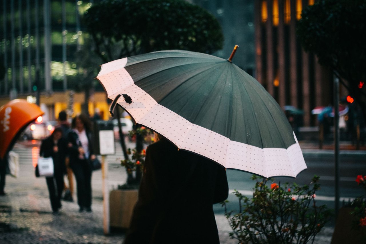 Pessoa caminhando com guarda-chuva em uma rua de São Paulo durante um dia chuvoso.
