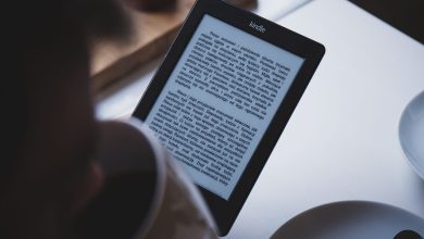 Pessoa lê em um leitor digital Kindle enquanto segura uma xícara de café, em ambiente interno.