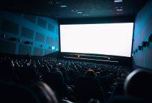 Público lotado sentado em uma sala de cinema enquanto assiste a um filme exibido em uma tela grande.