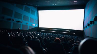 Público lotado sentado em uma sala de cinema enquanto assiste a um filme exibido em uma tela grande.