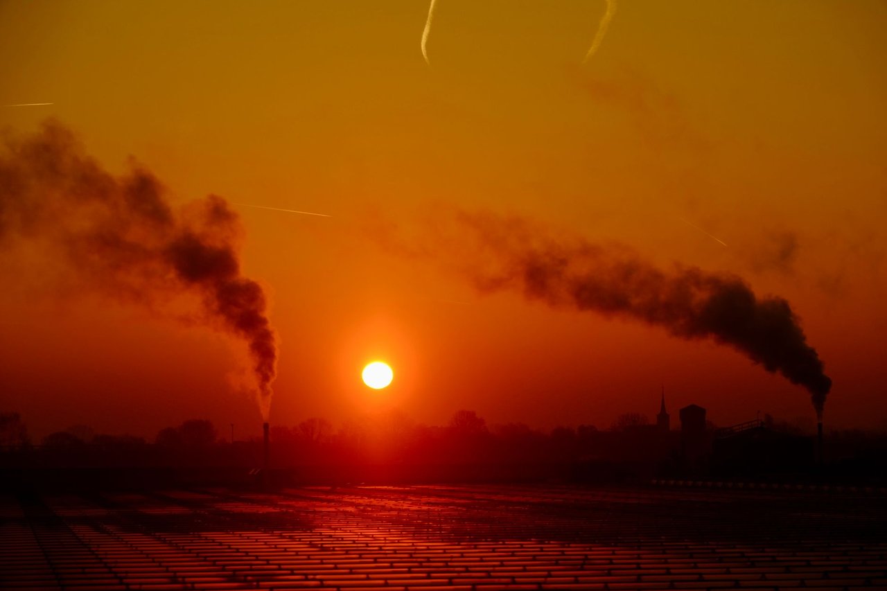 Chaminés de um complexo industrial emitindo fumaça sobre a paisagem ao entardecer.