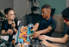 Três engenheiros colaboram diante de equipamentos industriais em uma fábrica moderna.