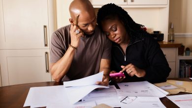 Casal analisa documentos e usa um celular enquanto administra as finanças domésticas à mesa.