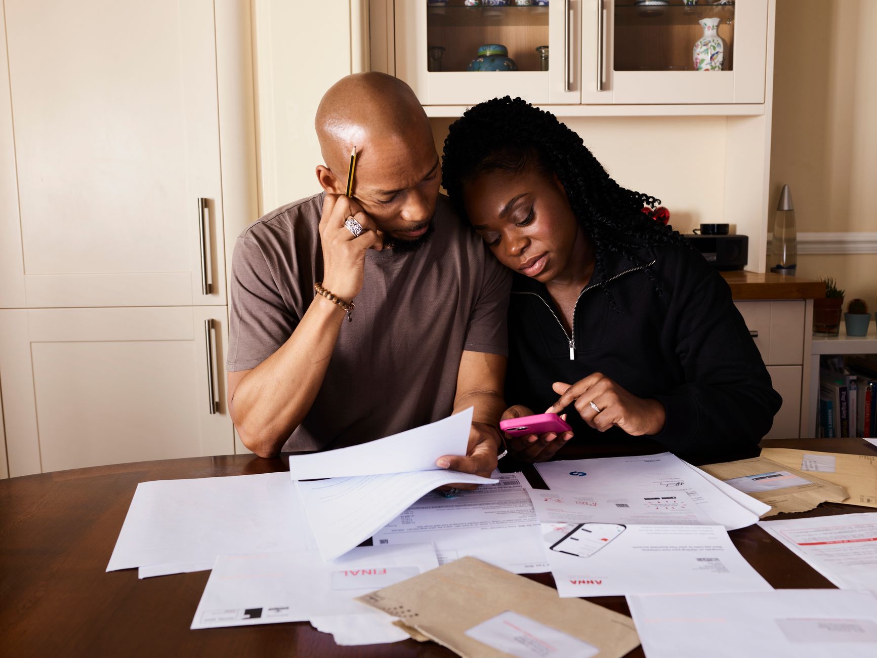 Casal analisa documentos e usa um celular enquanto administra as finanças domésticas à mesa.